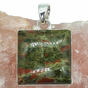 May include: A square green and red gemstone pendant with a silver bail. The gemstone has a mottled pattern of green and red.