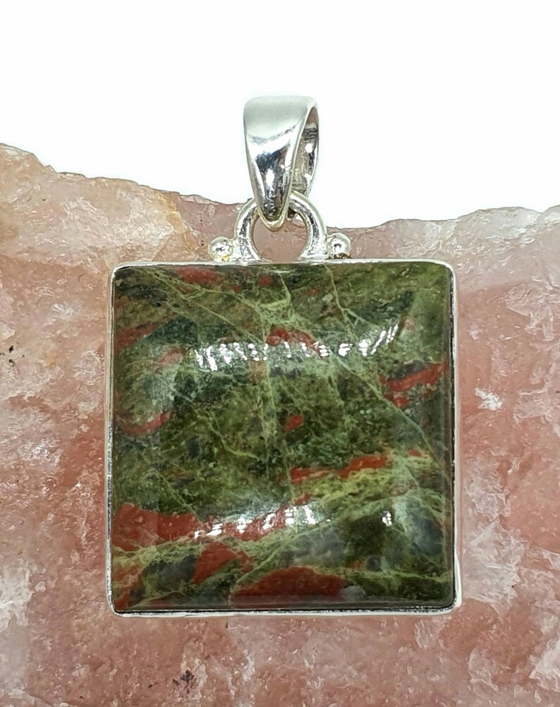 May include: A square green and red gemstone pendant with a silver bail. The gemstone has a mottled pattern of green and red.