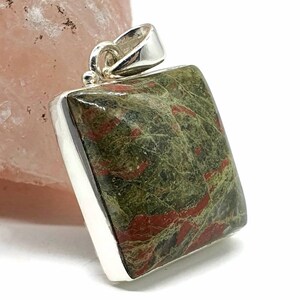 May include: A square pendant with a green and red jasper stone set in sterling silver. The stone has a unique pattern of red and green swirls.