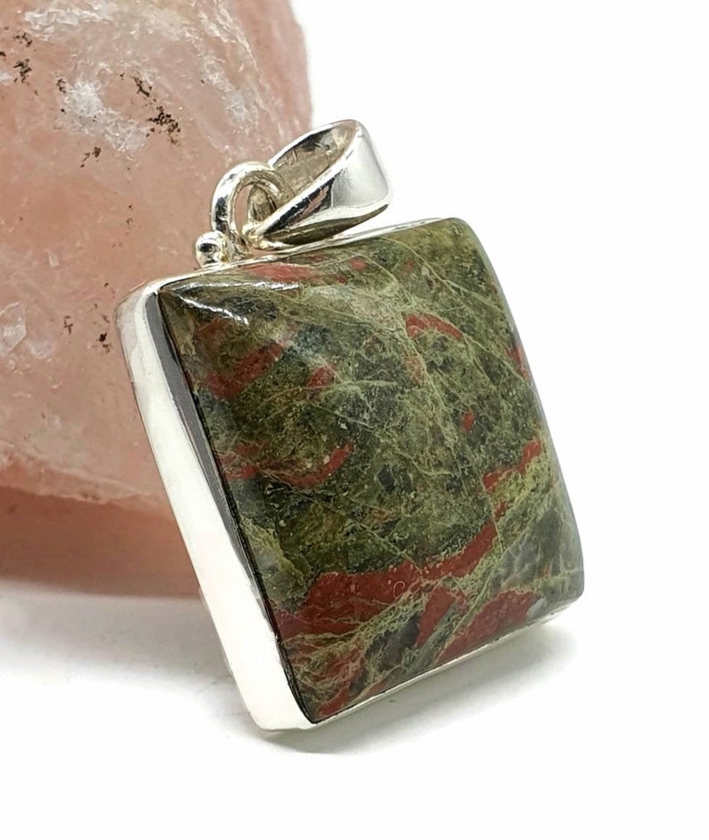 May include: A square pendant with a green and red jasper stone set in sterling silver. The stone has a unique pattern of red and green swirls.