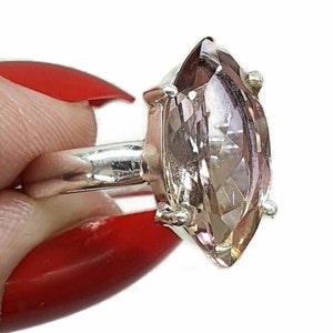 May include: A silver ring with a large, clear, marquise-shaped gemstone. The gemstone has a light pink hue.