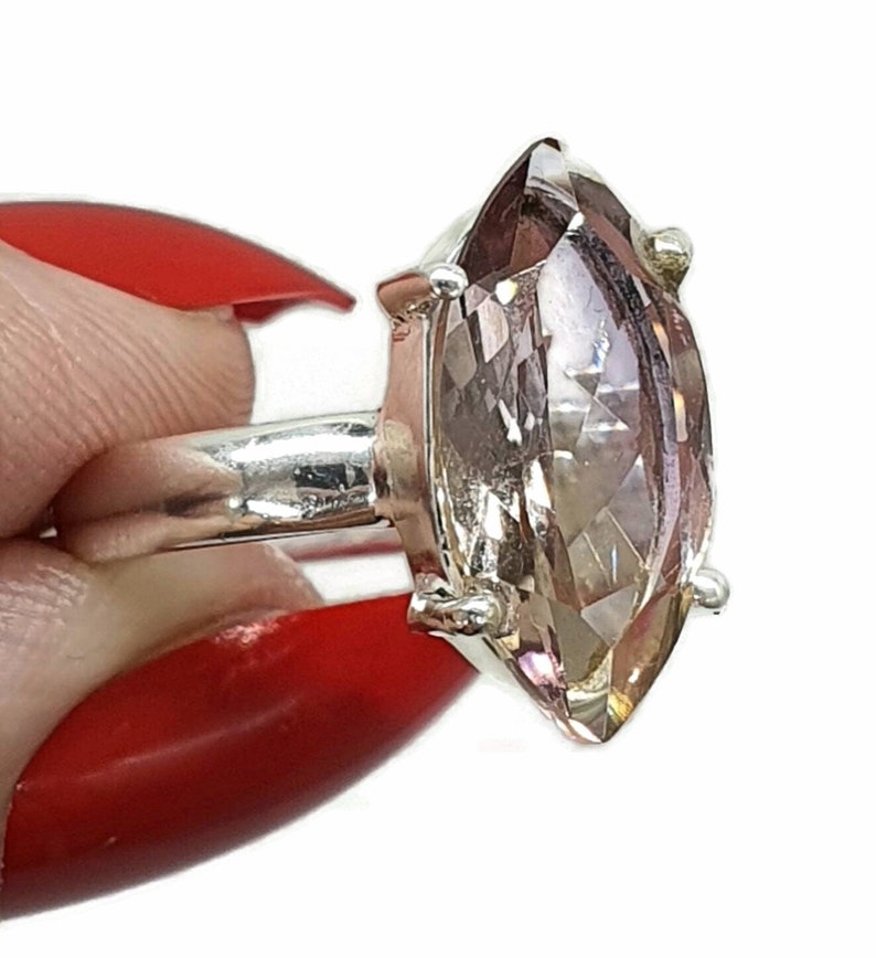 May include: A silver ring with a large, clear, marquise-shaped gemstone. The gemstone has a light pink hue.