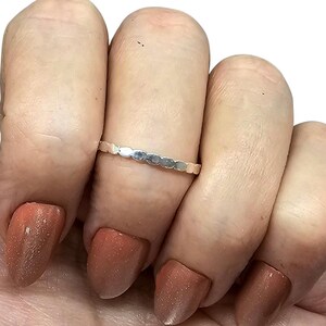 Puede incluir: Un anillo plateado con un dise&ntilde;o festoneado repetido. El anillo se lleva en un dedo con u&ntilde;as pulidas de color marr&oacute;n rojizo. El delicado dise&ntilde;o del anillo a&ntilde;ade un toque de elegancia a la mano.