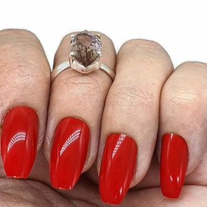 May include: A silver ring with a large, faceted, light brown gemstone. The ring is on a finger with red nail polish.