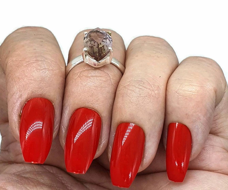 May include: A silver ring with a large, faceted, light brown gemstone. The ring is on a finger with red nail polish.