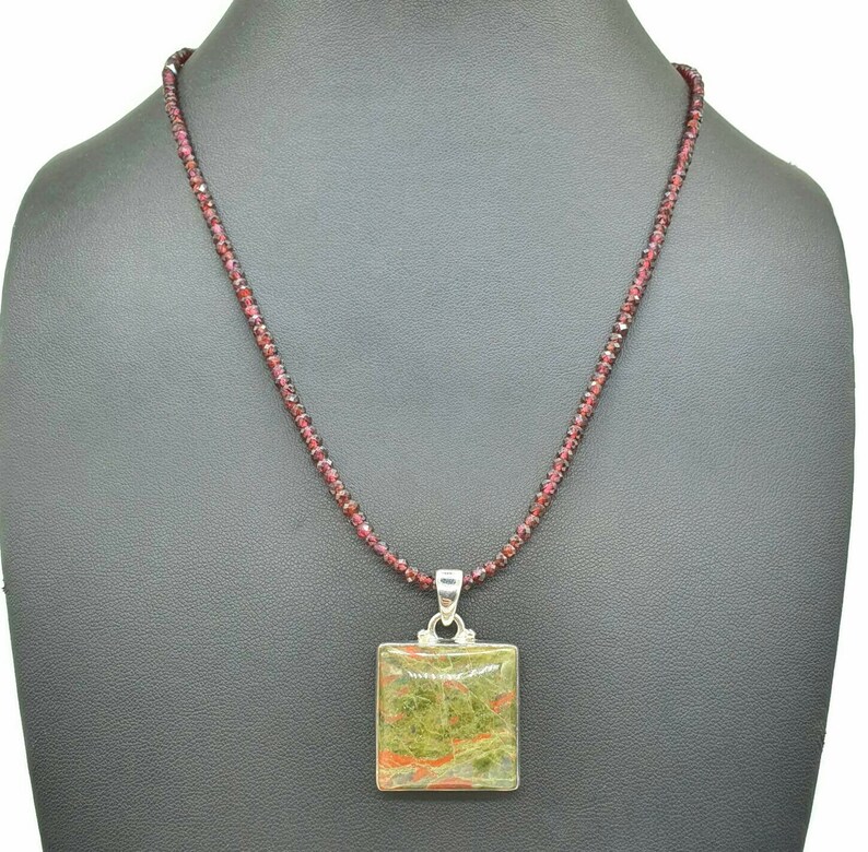 May include: A silver necklace with a square green, red, and brown stone pendant. The necklace is made of small red beads.