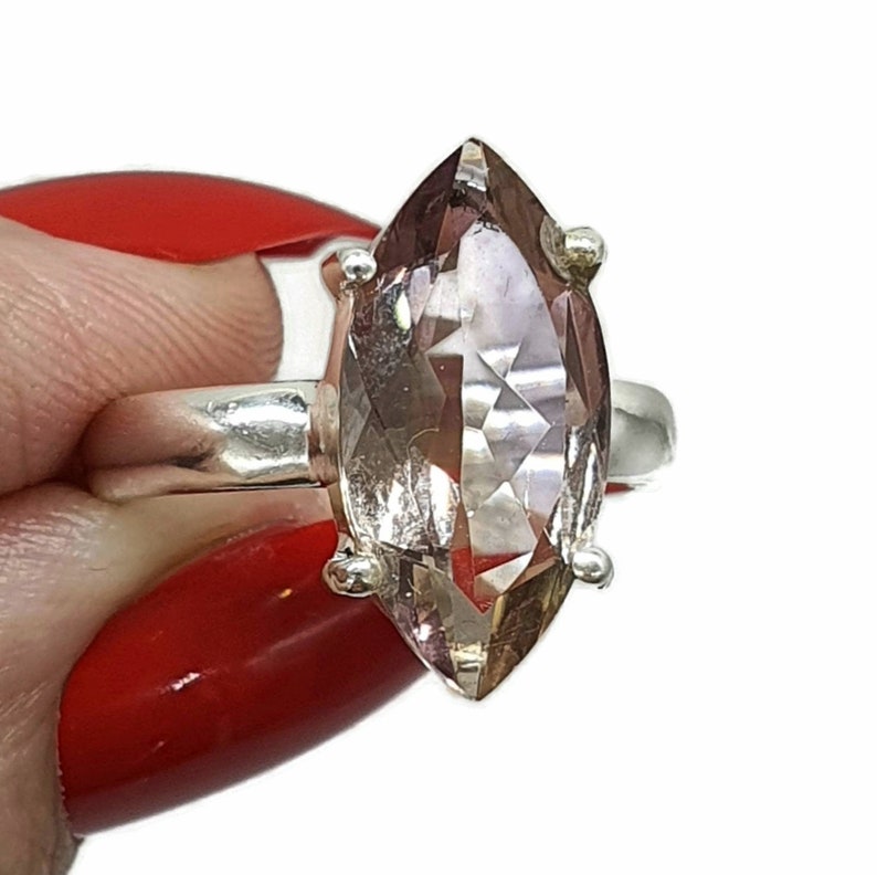 May include: A silver ring with a large, clear, marquise-shaped amethyst gemstone. The gemstone has a light purple hue and is set in a silver band.