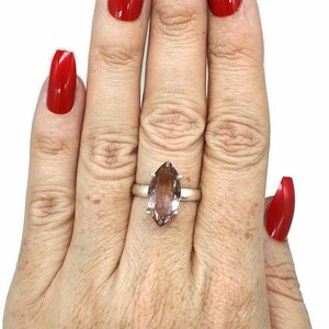 May include: A silver ring with a large, marquise-shaped amethyst gemstone. The ring is on a person's finger, and the person's nails are painted red.
