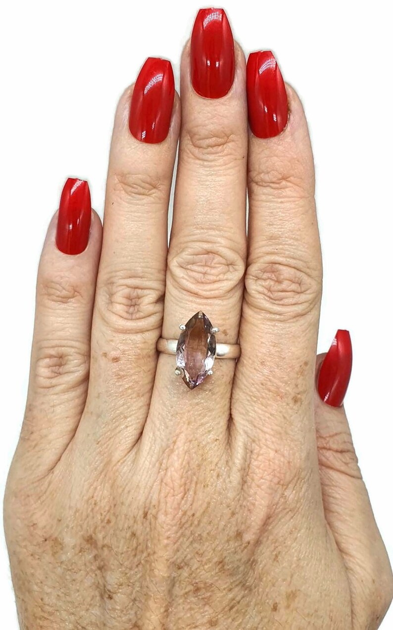 May include: A silver ring with a large, marquise-shaped amethyst gemstone. The ring is on a person's finger, and the person's nails are painted red.