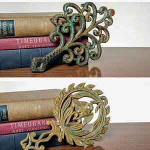 May include: Two antique metal trivets with ornate designs. The top trivet is green and the bottom trivet is gold. Both trivets are sitting on top of books.