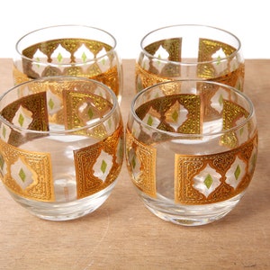 May include: Set of four clear glass tumblers with a gold and green geometric pattern. The glasses have a rounded shape and a wide base.