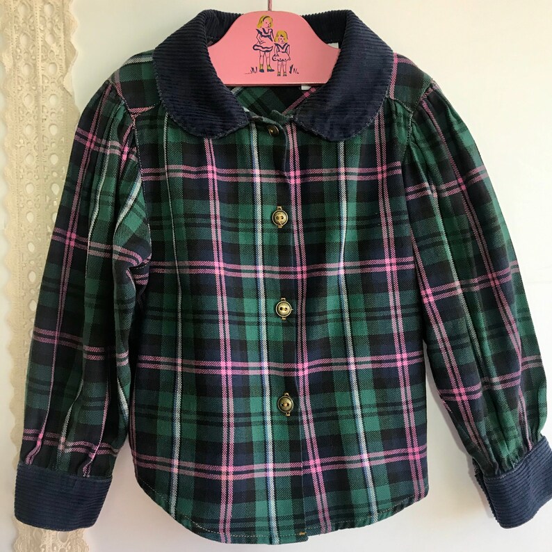 May include: A green and pink plaid shirt with a navy blue corduroy collar. The shirt has a button-up front and long sleeves.