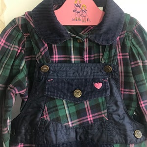 May include: A blue overall dress with a green and pink plaid shirt. The overall dress has a corduroy patch pocket with a pink heart on it. The shirt has a navy blue corduroy collar.