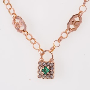 Op de afbeelding: Een gouden kettingarmband met een vierkante hanger met een groene edelsteen omringd door kleinere heldere edelstenen.