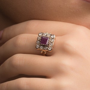 May include: A gold ring featuring a square ruby gemstone surrounded by smaller diamonds.