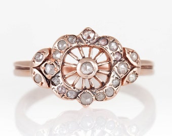 Può includere: Un anello in oro rosa con un delicato design traforato che presenta un diamante centrale circondato da diamanti più piccoli.