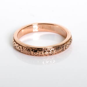 May include: A rose gold wedding band with an intricate floral design.