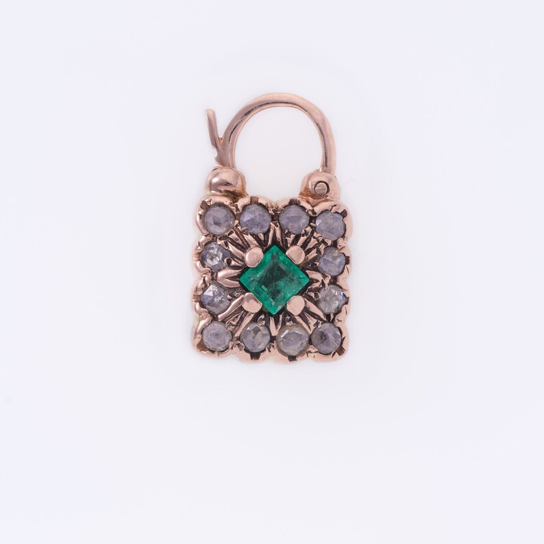 Op de afbeelding: Een gouden hangslotbedel met een groene smaragd in het midden en kleine diamanten eromheen.