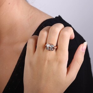 May include: A silver ring with a flower design featuring five white gemstones and red accents.
