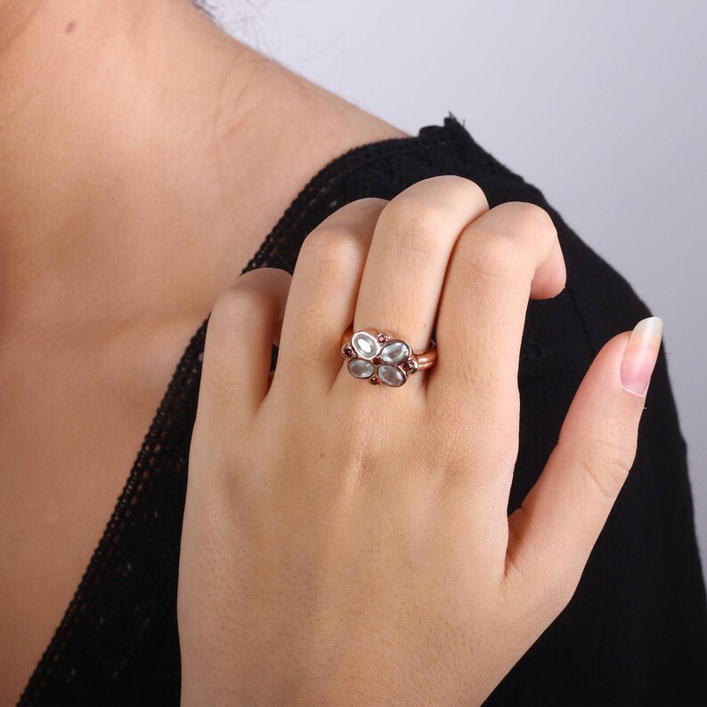 May include: A silver ring with a flower design featuring five white gemstones and red accents.