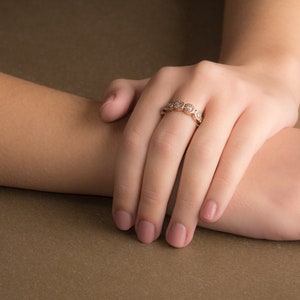 May include: A close-up of a woman's hand wearing a delicate gold ring with small round diamonds. The ring is on the ring finger of her right hand.