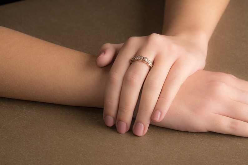May include: A close-up of a woman's hand wearing a delicate gold ring with small round diamonds. The ring is on the ring finger of her right hand.