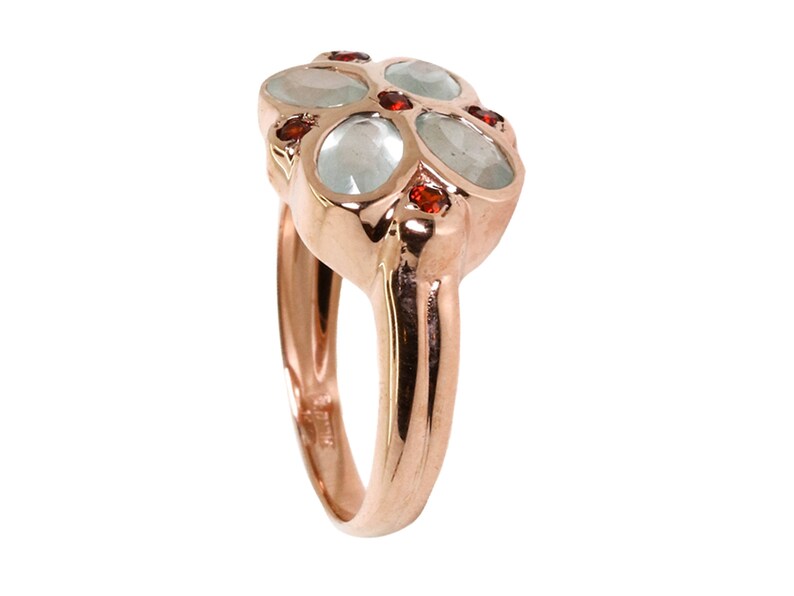 May include: A rose gold ring with five oval-shaped gemstones. The center stone is larger and surrounded by four smaller stones. The smaller stones are red, and the larger stone is a light blue color.