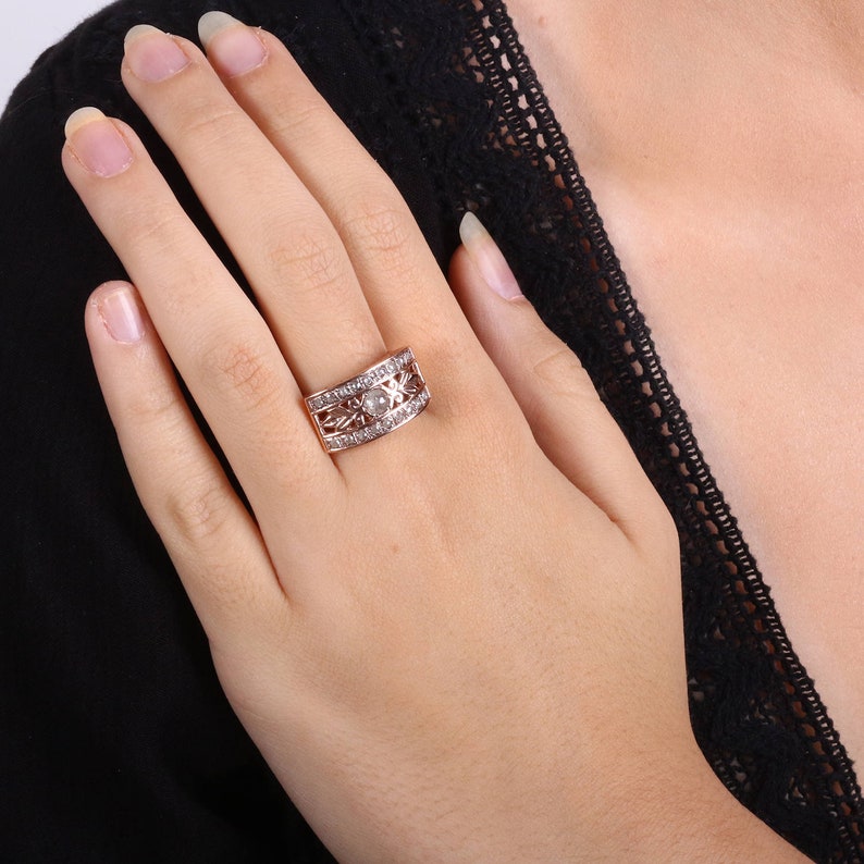 May include: A rose gold ring with a large, clear center stone surrounded by smaller stones. The ring has a delicate, intricate design.