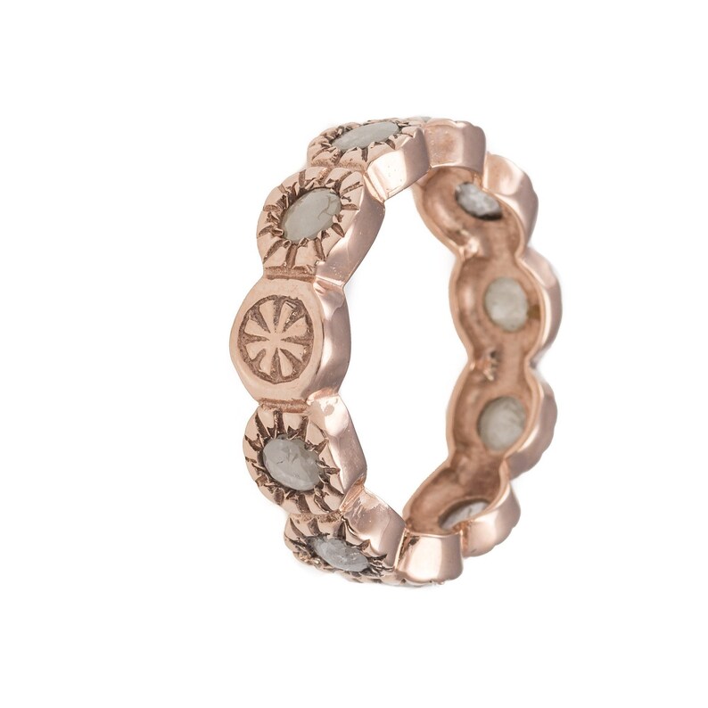 May include: A rose gold band ring with a row of round, clear stones set in a decorative, textured design.