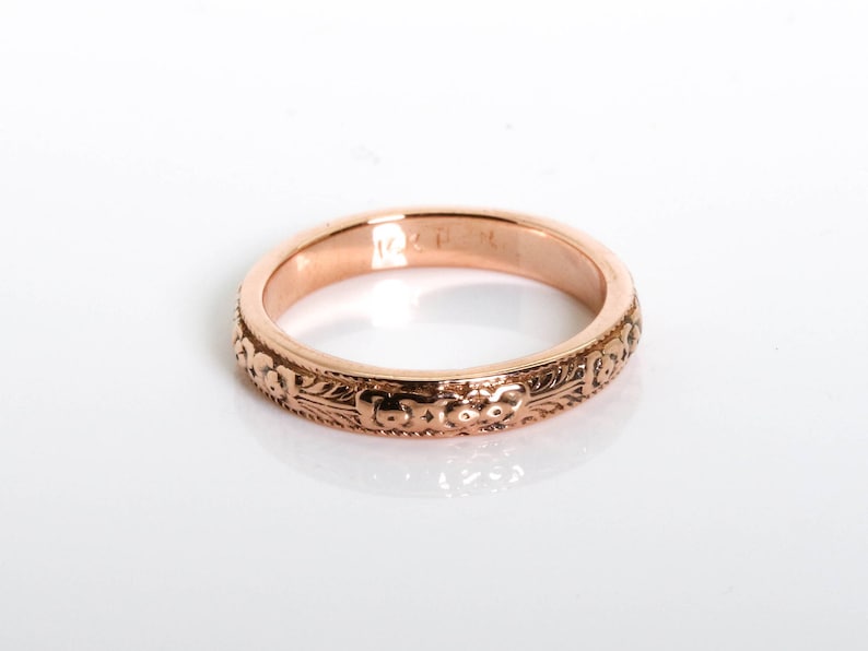 May include: A rose gold wedding band with an intricate floral design.