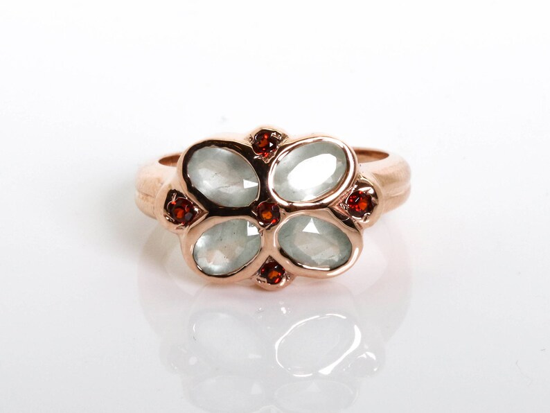 May include: A rose gold ring with five oval-shaped white gemstones and six small red gemstones.