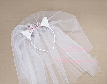 Puede incluir: Velo de novia blanco con una diadema blanca con orejas de gato de purpurina rosa y la palabra "Bride" en la diadema.