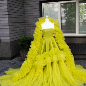 May include: A bright yellow tulle dress with a ruffled skirt and a long, flowing train. The dress is strapless and has a fitted bodice.