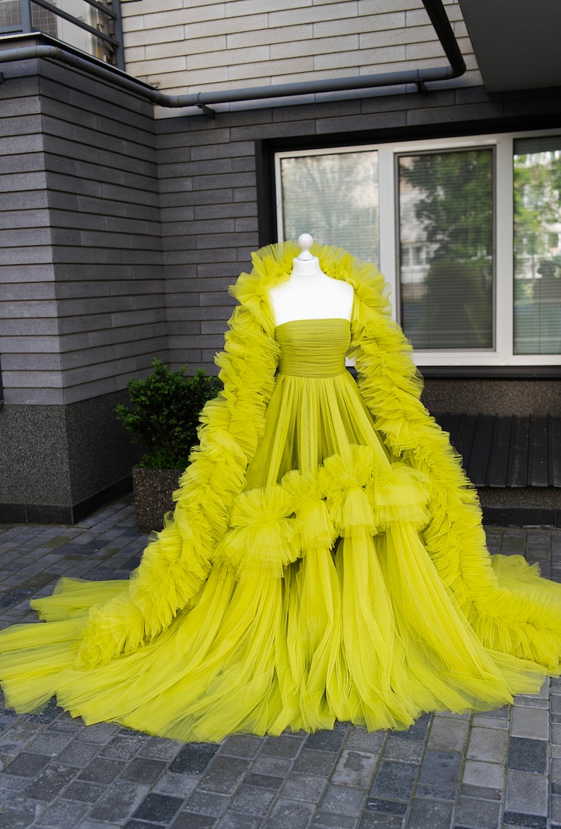 May include: A bright yellow tulle dress with a ruffled skirt and a long, flowing train. The dress is strapless and has a fitted bodice.