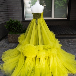 May include: A bright yellow tulle ball gown with a fitted bodice and a full skirt. The skirt has multiple layers of tulle and features large ruffles around the bottom.