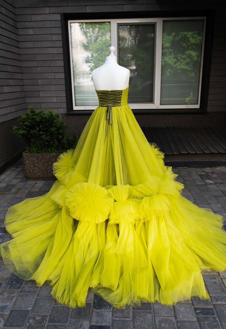 May include: A bright yellow tulle ball gown with a fitted bodice and a full skirt. The skirt has multiple layers of tulle and features large ruffles around the bottom.