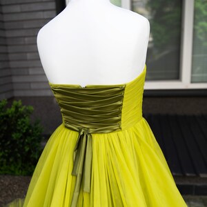 May include: A strapless tulle gown in a bright yellow color with a green satin sash tied in a bow at the back.
