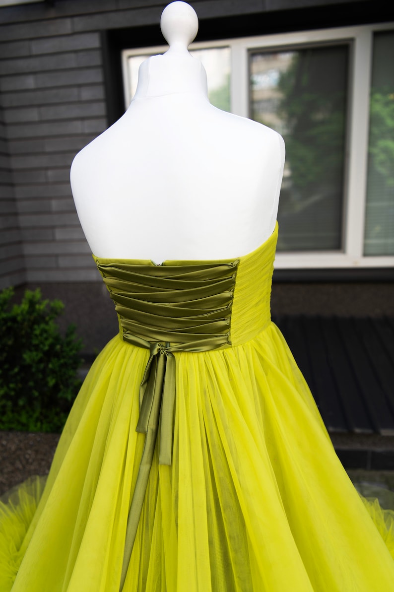 May include: A strapless tulle gown in a bright yellow color with a green satin sash tied in a bow at the back.