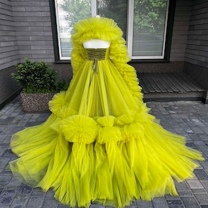May include: A bright yellow tulle gown with a ruffled bodice and skirt. The gown has a fitted bodice with a satin ribbon tie at the waist. The skirt is full and flowing with multiple layers of tulle.