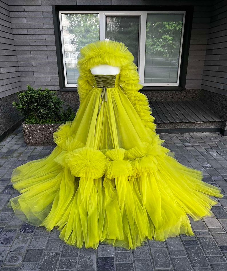 May include: A bright yellow tulle gown with a ruffled bodice and skirt. The gown has a fitted bodice with a satin ribbon tie at the waist. The skirt is full and flowing with multiple layers of tulle.