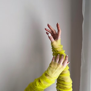 May include: A pair of bright yellow mesh long sleeves with ruched detailing. The sleeves are worn on a person's arms, with the hands visible.