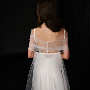 Puede incluir: Un vestido de novia de tul blanco con la espalda baja y una superposici&oacute;n transparente. El vestido tiene una fila de botones en la espalda y una falda fluida.