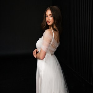 Puede incluir: Un vestido de novia de tul blanco con un corpi&ntilde;o de sat&eacute;n y una superposici&oacute;n transparente. El vestido tiene un escote de coraz&oacute;n y un corpi&ntilde;o ajustado. La falda es completa y fluida.