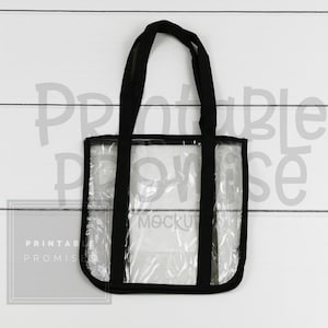 Puede incluir: Bolso tote transparente con asas y ribetes negros. La bolsa está hecha de material transparente, lo que permite ver el contenido. La bolsa tiene forma rectangular y está diseñada para transportar artículos. El texto "Mockup" es visible dentro de la bolsa.