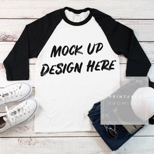 May include: White baseball tee with black sleeves, a black and white graphic that says "Mock Up Design Here", blue jeans, sunglasses, and a white baseball cap.