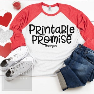 May include: A mock-up featuring a white and red raglan-style long-sleeve shirt with the text "Printable Promise Mockups" in black. The image includes a pair of white sneakers, blue jeans, and heart-shaped decorations.