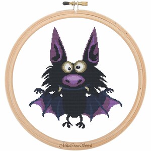 May include: Cross stitch pattern of a purple and black cartoon bat with big eyes and fangs in a wooden embroidery hoop. The hoop has the text "MilaCross Stitch" on the bottom.