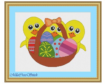 May include: Cross-stitch artwork featuring three yellow chicks surrounding a brown basket filled with colorful Easter eggs. The chicks have large eyes and orange beaks. A light blue border frames the image, with a gold-colored frame.
