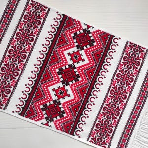 May include: White fabric with a red and black embroidered geometric pattern. The pattern is a traditional Ukrainian design.