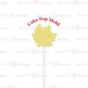May include: A yellow cake pop mold in the shape of a maple leaf. The mold is on a white stick and is ready to be used to make cake pops.
